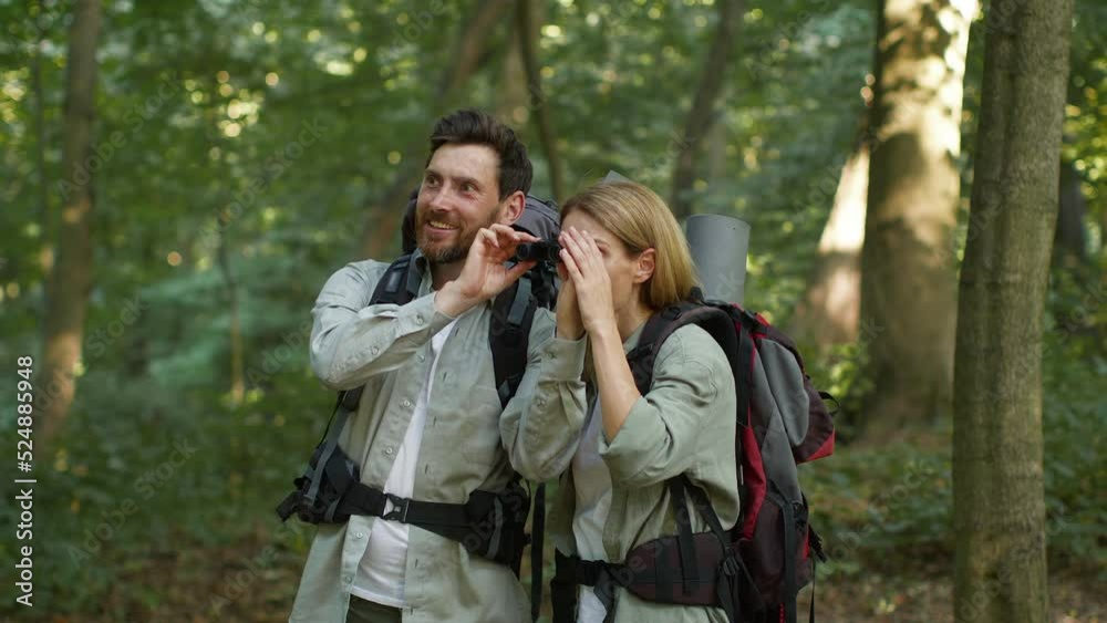 Couple of two happy middle aged tourists travelling in woodland, looking forward through binoculars, free space