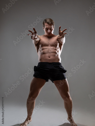 Muscular man in an artistic pose, portrait on a gray background. An athlete guy with spectacular muscles poses like an antique hero