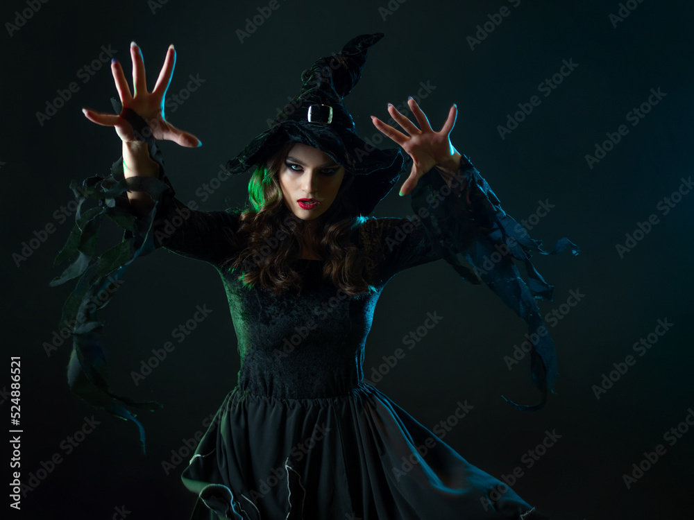 beautiful witch with hat make spell. Halloween party, witches ' Sabbath. Young beautiful brunette in witch costume, greenish backlight, dark background