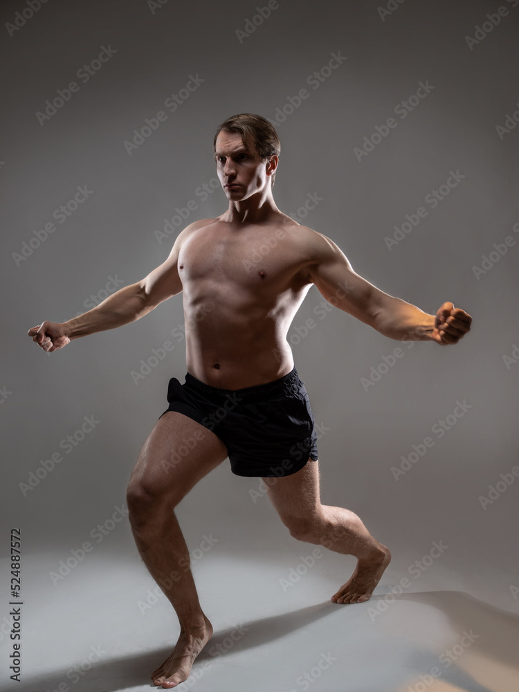 Obraz premium young muscular man in an expressive pose, artistic pose of the hero with outstretched arms. Beautiful muscles. extraordinary athletic body. Portrait on a gray background