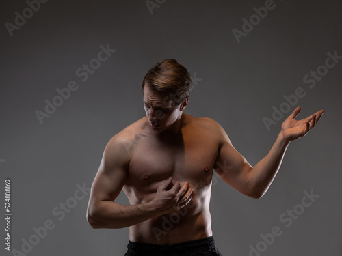 A muscular man expressively emotionally poses on a gray background. The guy is an athlete with pumped-up muscles. beautiful body relief.