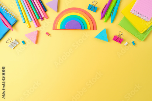 Back to school concept with notebooks, pens and rainbow sticky notes on yellow background. Top view, flat lay