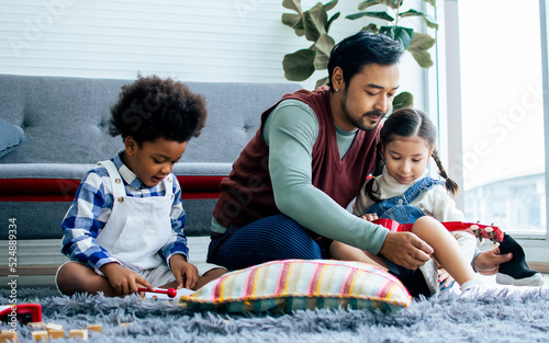 Single handsome father taking care with love to adopted children who are little diverse Caucasian, African girl and boy, sitting on floor in living room at home. Lifestyle, family, kids Concept.