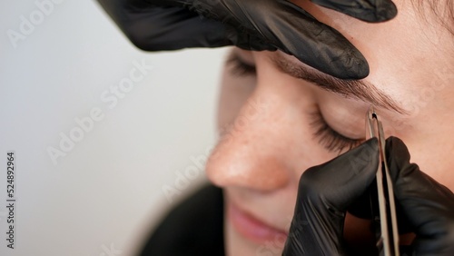 beauty saloon. close-up  hands of the cosmetician in black rubber gloves hold tweezers and pull out eyebrows. Master corrects the shape of the eyebrows. High quality photo