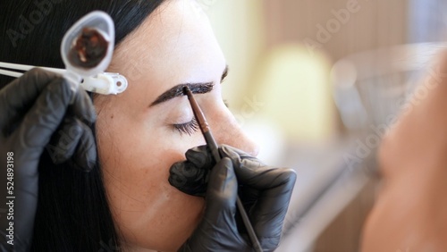 close up. young woman gets eyebrow correction procedure. kosmetolog- makeup artist applies paint with brush on eyebrows in beauty saloon. Professional care for face. High quality photo photo