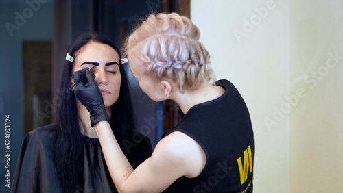 young woman gets eyebrow correction procedure. kosmetolog- makeup artist applies paint with brush on eyebrows in beauty saloon. Professional care for face. High quality photo photo