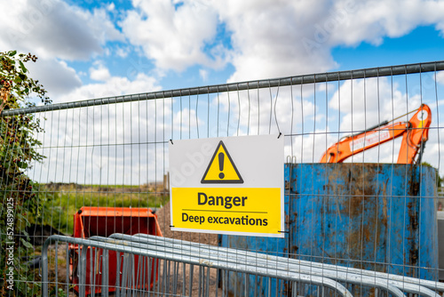 Generic yellow triangle warning sign describing Deep Excavations at a pipeline laying site. Beyond the fence its a 20ft deep hole which poses a hazard to the public.