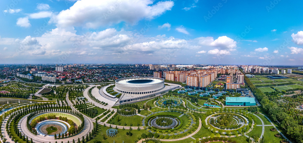 city park in the north-east of Krasnodar (South of Russia) with many round and oval flower beds, photo location objects and a large stadium surrounded by high-rise buildings - aerial panorama