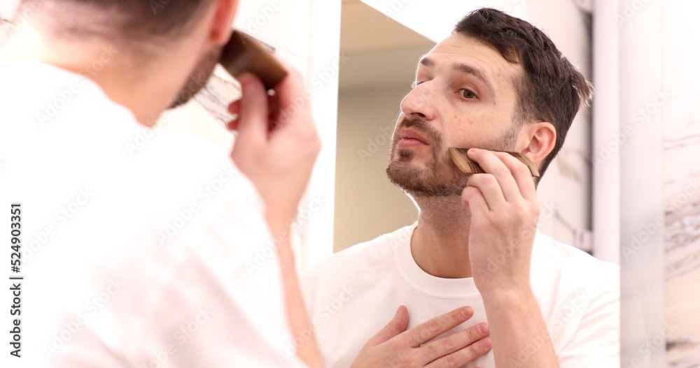 Hipster man focusing on combing beard in front of a mirror. Hipster man focusing on combing beard in front of a mirror.