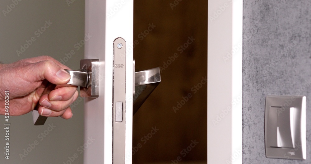 To open the door. Modern white door with chrome metal handle and a man's arm. Elements of interior closeup.