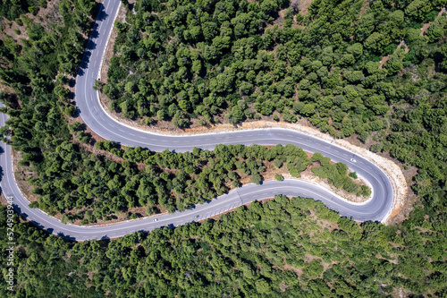 Aerial top view of curves at a highway through thick pine forest as seen on the island of Evia, Greece