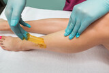 Woman undergoing leg hair removal procedure with sugaring paste in salon