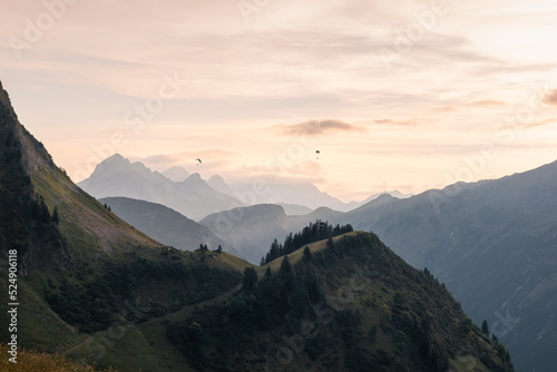 View from the Enzianhütte to the Allgäu mountains at sunset with two paragliding in the air.