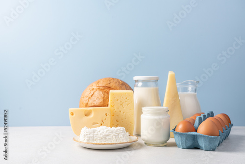 Variety of dairy products on blue background. Jug of milk, cheese, butter, yogurt or sour cream, cottage cheese, bread and eggs. Farm dairy products concept photo