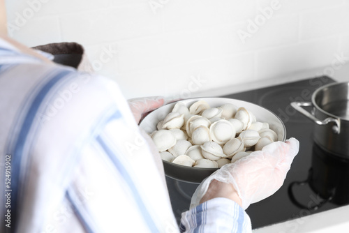 Woman holding bowl of delicious dumplings in kitchen, closeup