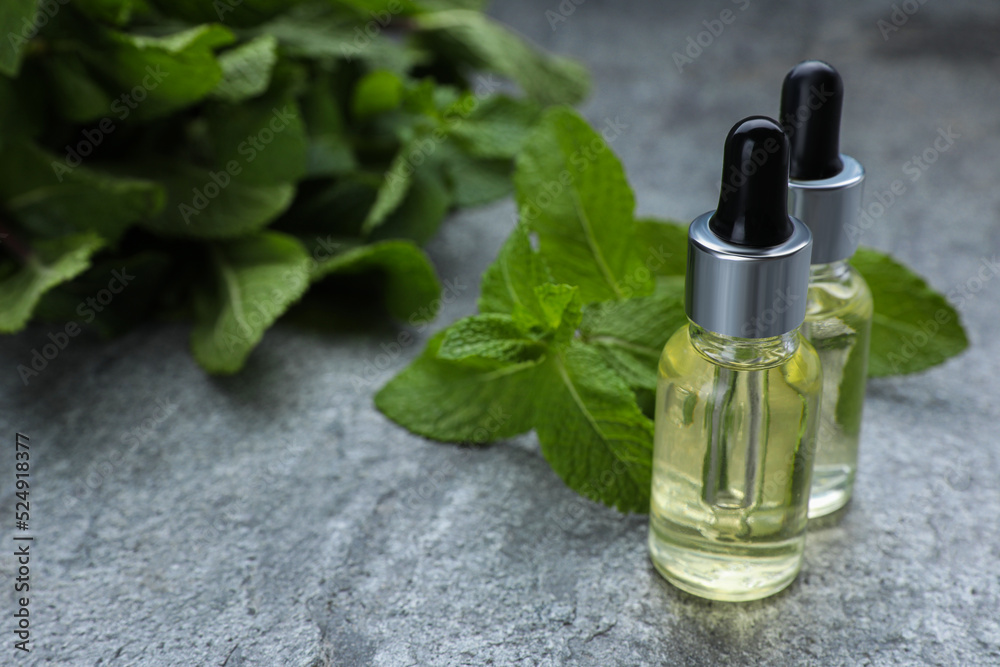Bottles of essential oil and mint on grey table, closeup. Space for text Bottles of essential oil and mint on grey table, closeup. Space for text