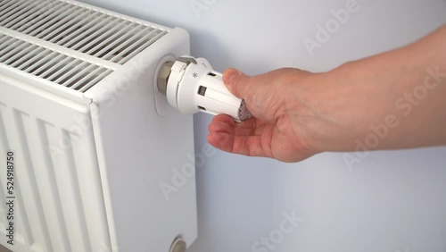 A woman's hand adjusts the thermostat on the heater. The concept of economical use of resources. Poor heating in winter.