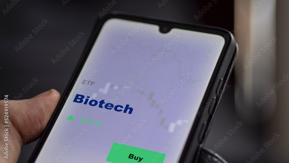 An investor's analyzing the biotech etf fund on screen. A phone shows the ETF's prices bio tech shares to invest An investor's analyzing the biotech etf fund on screen. A phone shows the ETF's prices bio tech shares to invest