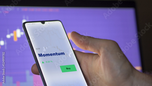 An investor's analyzing the momentum etf fund on screen. A phone shows the ETF's prices momentum to invest