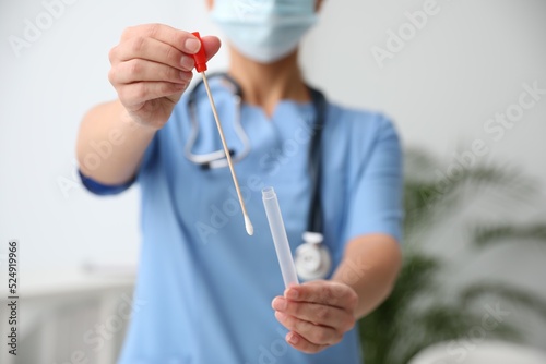 Doctor holding buccal cotton swab and tube for DNA test in clinic, closeup photo