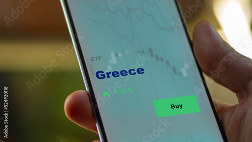 An investor's analyzing the Greece etf fund on screen. A phone shows the ETF's prices Greek greek greece to invest