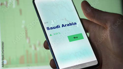 An investor's analyzing the Saudi Arabia etf fund on screen. A phone shows the ETF's prices Saudian to invest photo
