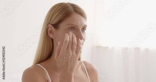 Smiling senior woman applying anti-aging lotion to remove dark circles under eyes