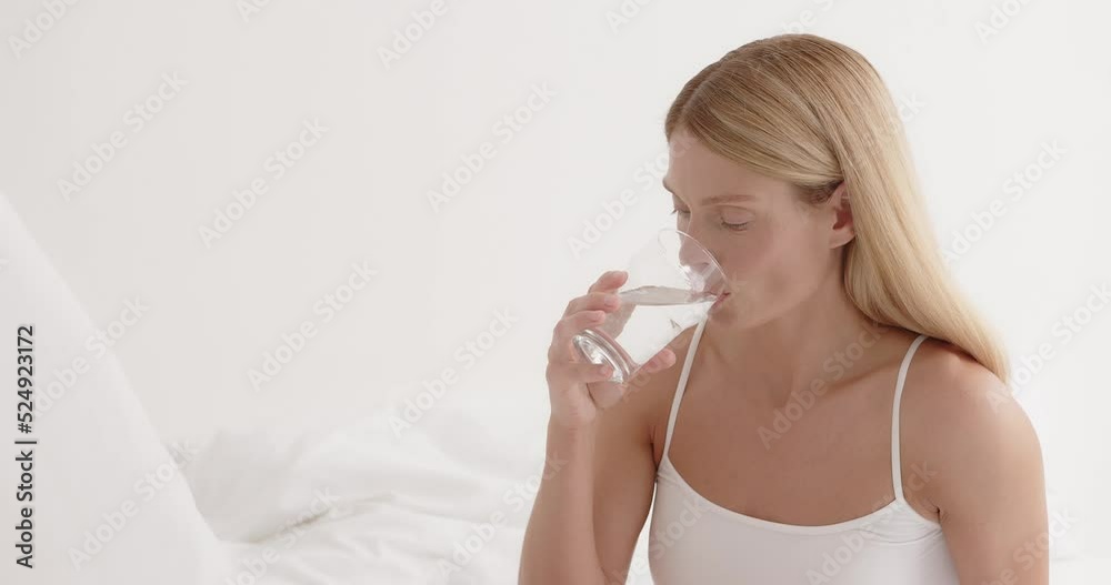 Senior attractive woman sit on bed, drink glass of water in bedroom Senior attractive woman sit on bed, drink glass of water in bedroom