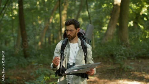 Active man tourist got lost during hiking trip in woodland, looking for right way with compass and paper map, free space