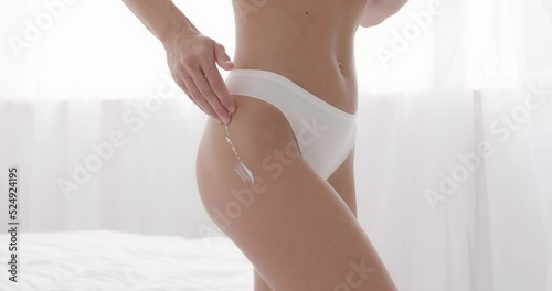 Woman smearing her thigh and buttocks with anti-cellulite moisturising cream