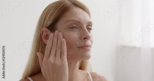 Happy mature woman using cosmetic cream to hide wrinkles below eyes