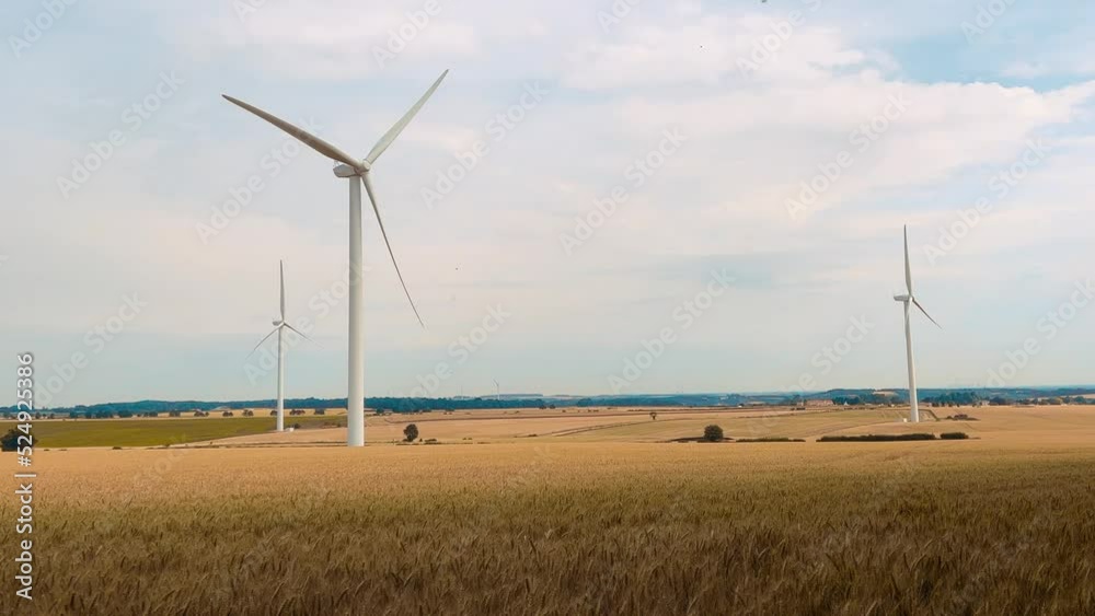 An electricity generating windmills on the gold wheat field against cloudy blue sky in England An electricity generating windmills on the gold wheat field against cloudy blue sky in England