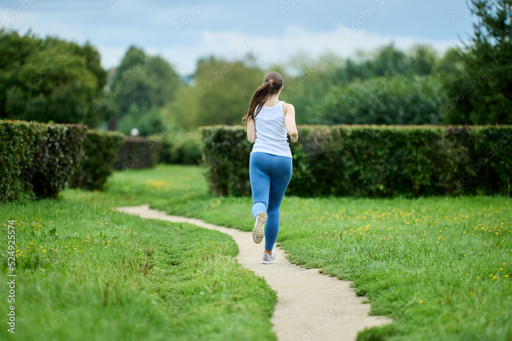 Female runner exercising in public park in summer, back view. Female runner exercising in public park in summer, back view.