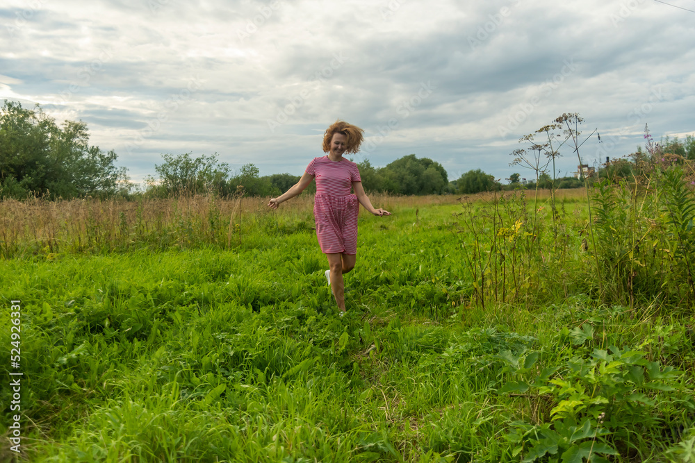 a girl with fluttering hair in the wind in a red dress runs through a meadow with green grass.