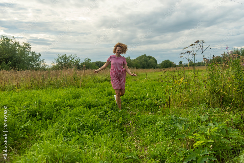 a girl with fluttering hair in the wind in a red dress runs through a meadow with green grass. a girl with fluttering hair in the wind in a red dress runs through a meadow with green grass.