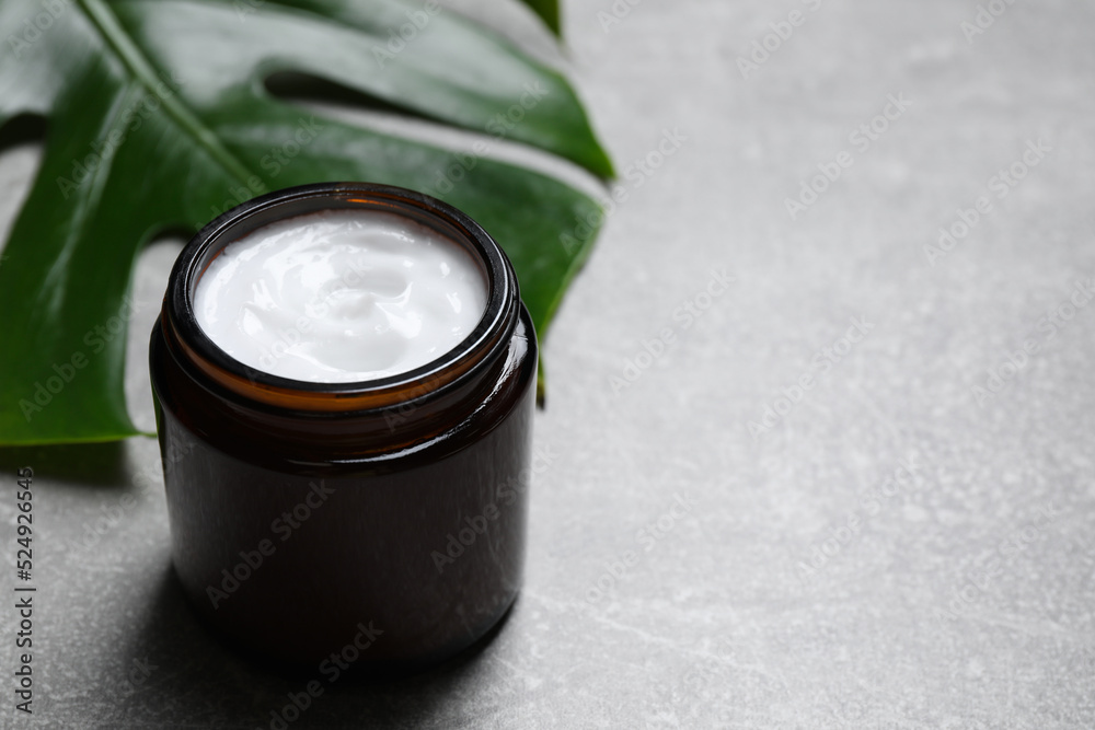 Jar of hand cream and green leaf on grey table, space for text Jar of hand cream and green leaf on grey table, space for text