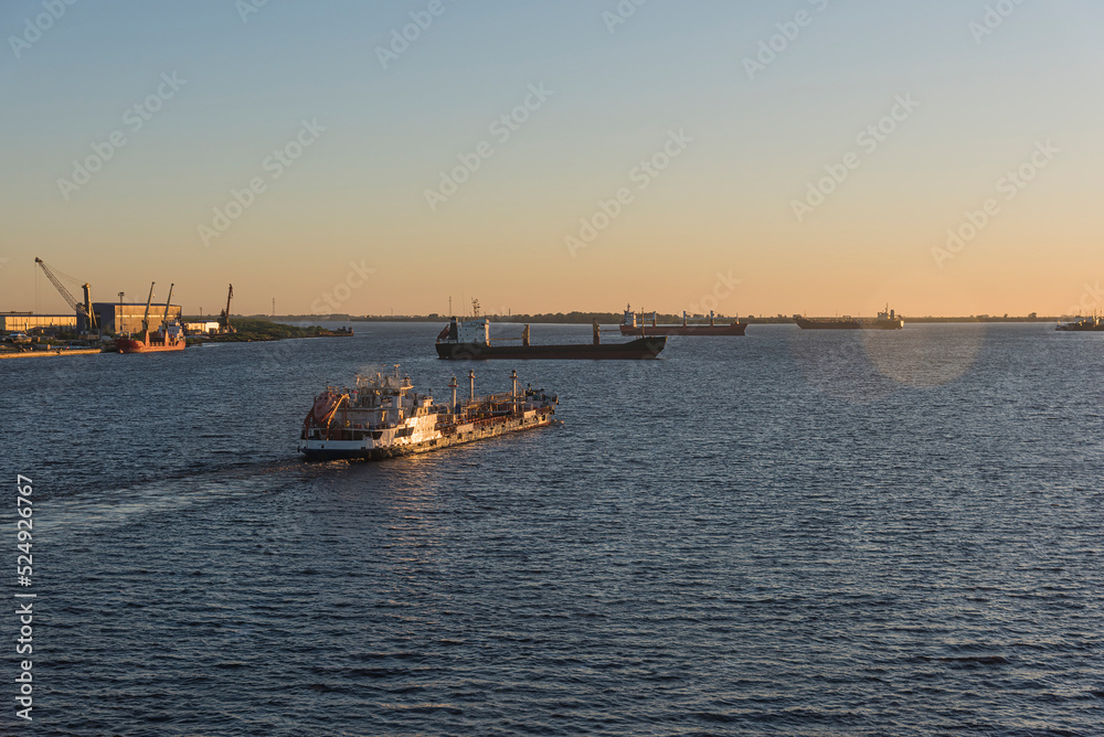 a tugboat sails along the wide Northern Dvina River in the northern part of Russia against the background of dry cargo ships standing in the roadstead