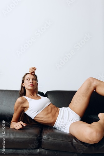 A woman with tanned skin lying on the couch in white linen, taking care of her health and body skin. Smooth body skin after waxing