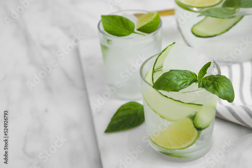 Tasty fresh cucumber water with sliced lime and basil on white marble table. Space for text