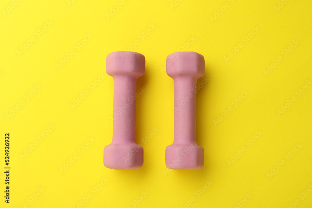 Stylish dumbbells on yellow background, flat lay Stylish dumbbells on yellow background, flat lay