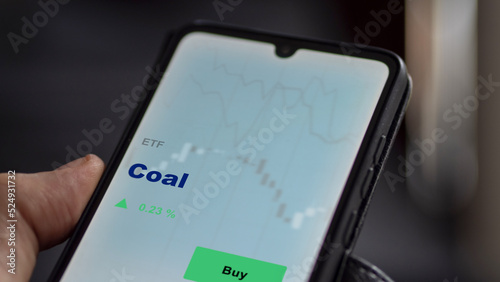 An investor's analyzing the coal etf fund on screen. A phone shows the ETF's prices energy carbon to invest