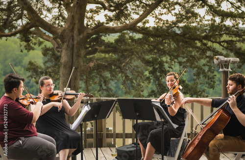 String quartet of two young men and two young women playing concert on wooden deck above Missouri River on summer evening; river and woods in background photo