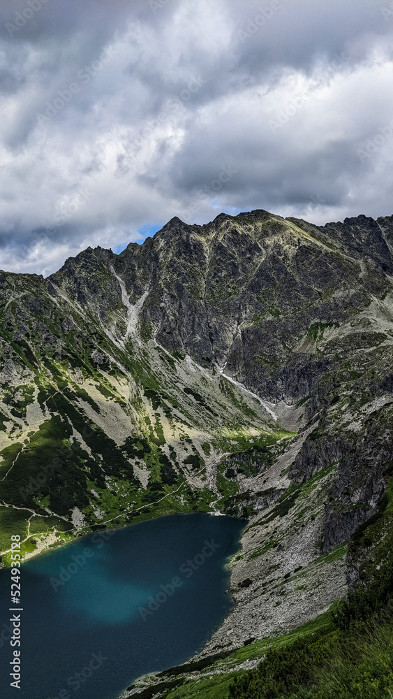 Beautiful landscape of lakes and mountains under the cloudy blue sky as wallpaper, poster or background. Incredible view of lakes and meadow under the mountains in the light of the sun. 