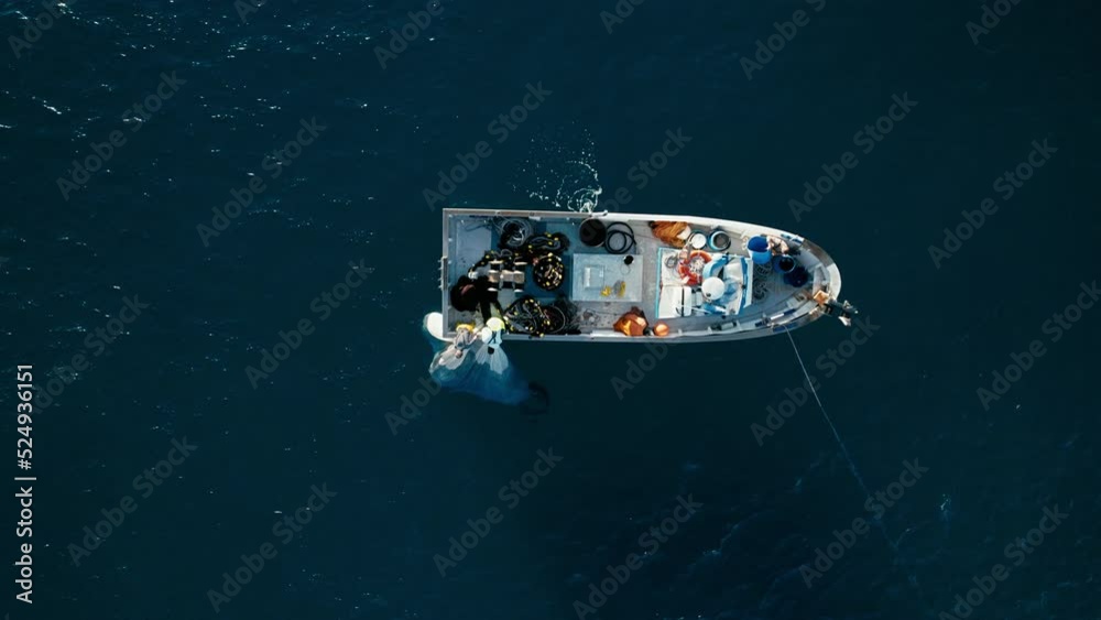 Fishermen crew work hard together pulling out net with caught sea fish on their trawler boat waving in blue waters ocean. Effective teamwork. Aerial top view shot