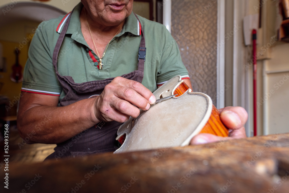 luthier carving the shape of the outside of the front of a violin with ...