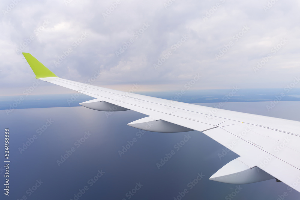 Obraz premium Wing of an airborne airplane ocean below. the plane flies over the water. clear blue sky. close up