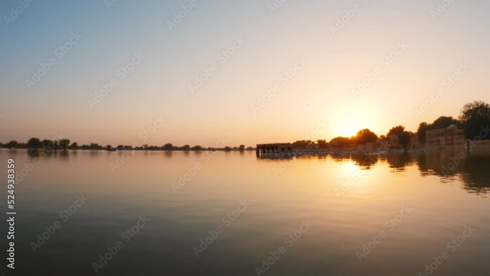 View of the Gadisar Lake during sunset with chhatri in the middle of the lake at Jaisalmer in Rajasthan, India. Reflection of the Chhatri pavilion in the orange water of the lake during sunset. View of the Gadisar Lake during sunset with chhatri in the middle of the lake at Jaisalmer in Rajasthan, India. Reflection of the Chhatri pavilion in the orange water of the lake during sunset.
