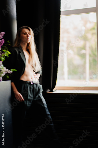 a sexy, beautiful blonde topless woman in a jacket in a dark room by the window.