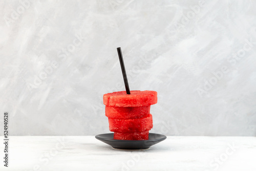 Watermelon slices in  with drinking straw on grey background.  Concept of refreshing cocktails and smoothies made from fresh watermelon pulp. Abstract cup