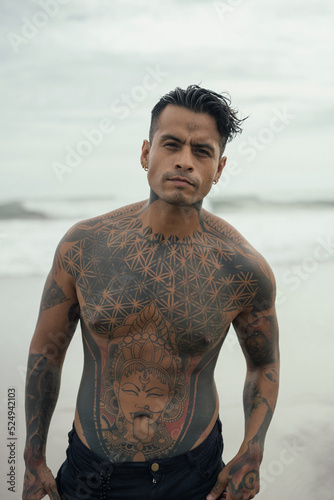Handsome tanned tattooed sexy man with a naked torso in a flying poreo on the ocean at sunset.
